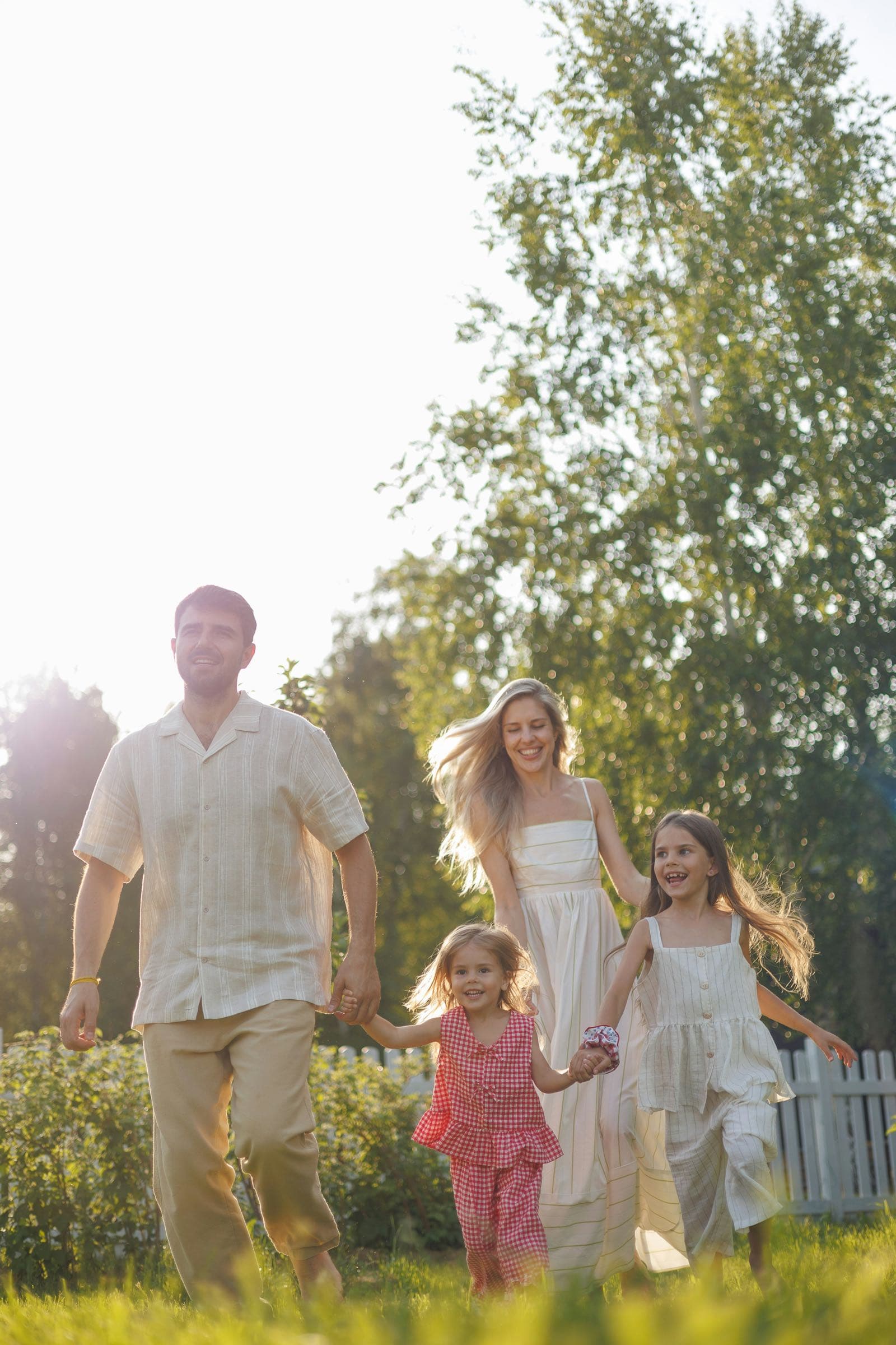 Parents and their two young daughters running together in a sunlit garden